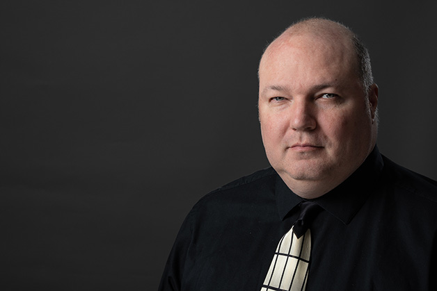 Male person in a dark shirt and tie on a dark background