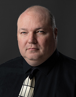 Male person in a dark shirt and tie on a dark background