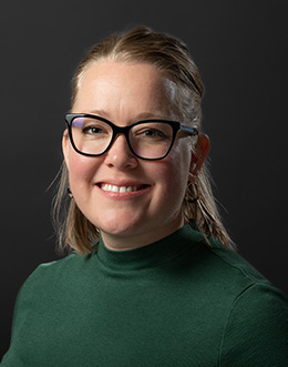 Female person in green shirt wearing glasses on dark background