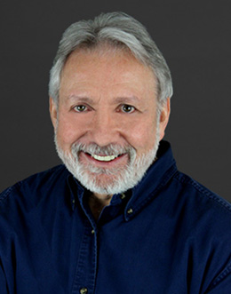 Male person with beard in dark shirt on dark background
