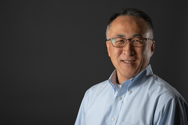 Male person wearing glasses in a light blue shirt on a dark background