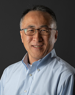 Male person wearing glasses in a light blue shirt on a dark background