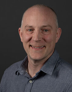 Male person in a gray shirt on a dark background