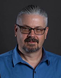 man wearing glasses in blue button shirt with dark background